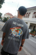 A man viewed from behind wearing a dark gray graphic t-shirt with 'EAT LAKSA RUN FASTA' printed on the back, set against an outdoor street background.