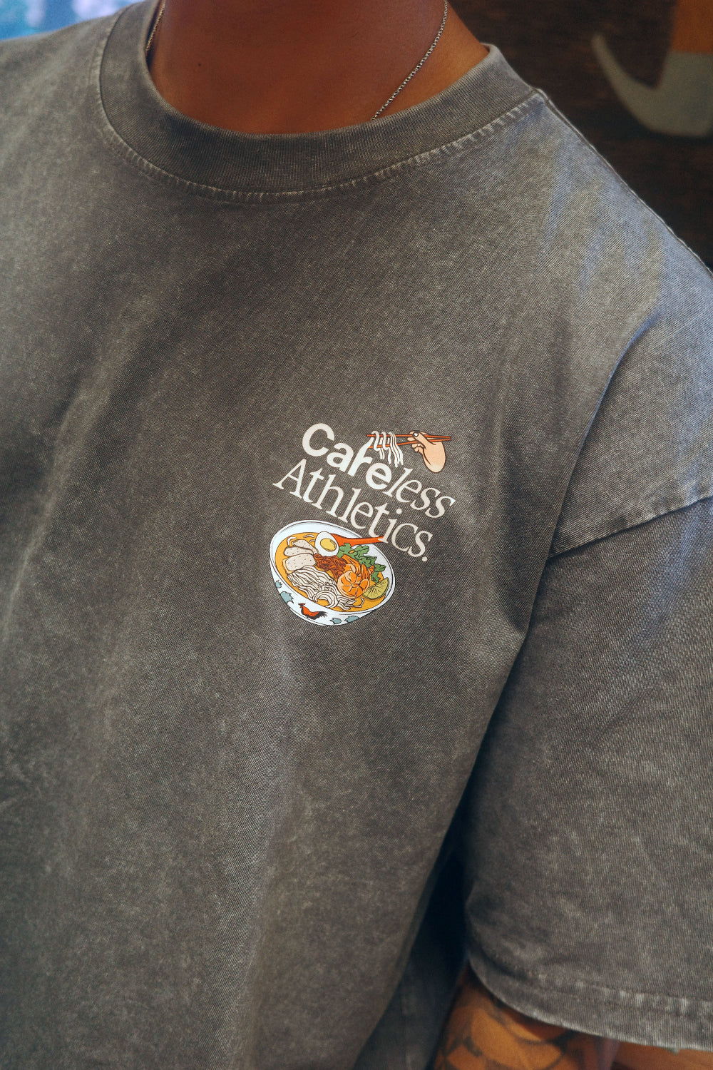 A close-up of a person wearing a faded dark gray t-shirt with a 'Careless Athletics' logo printed on the left chest.