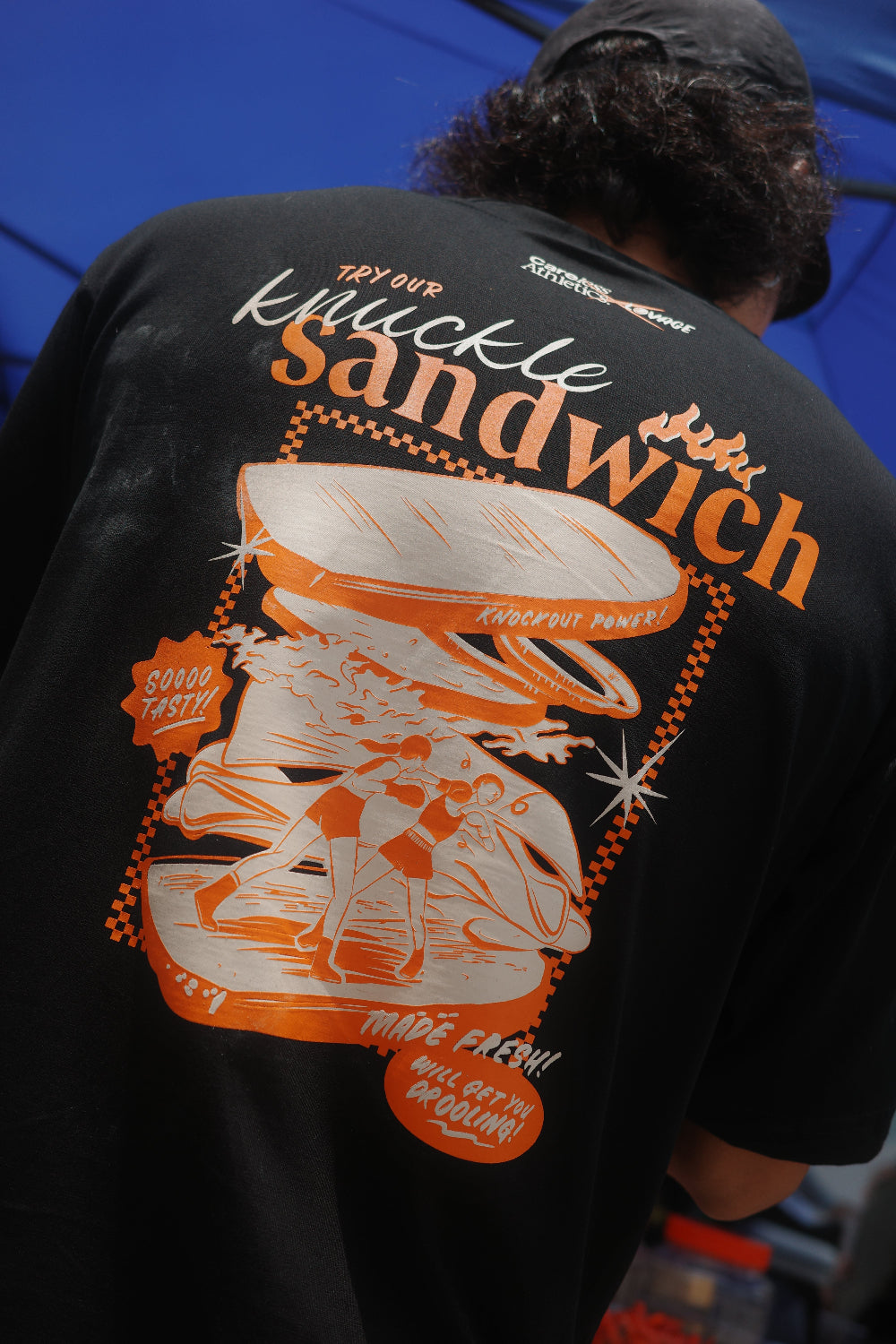 Person wearing a black sweatshirt with orange and white graphics and text.