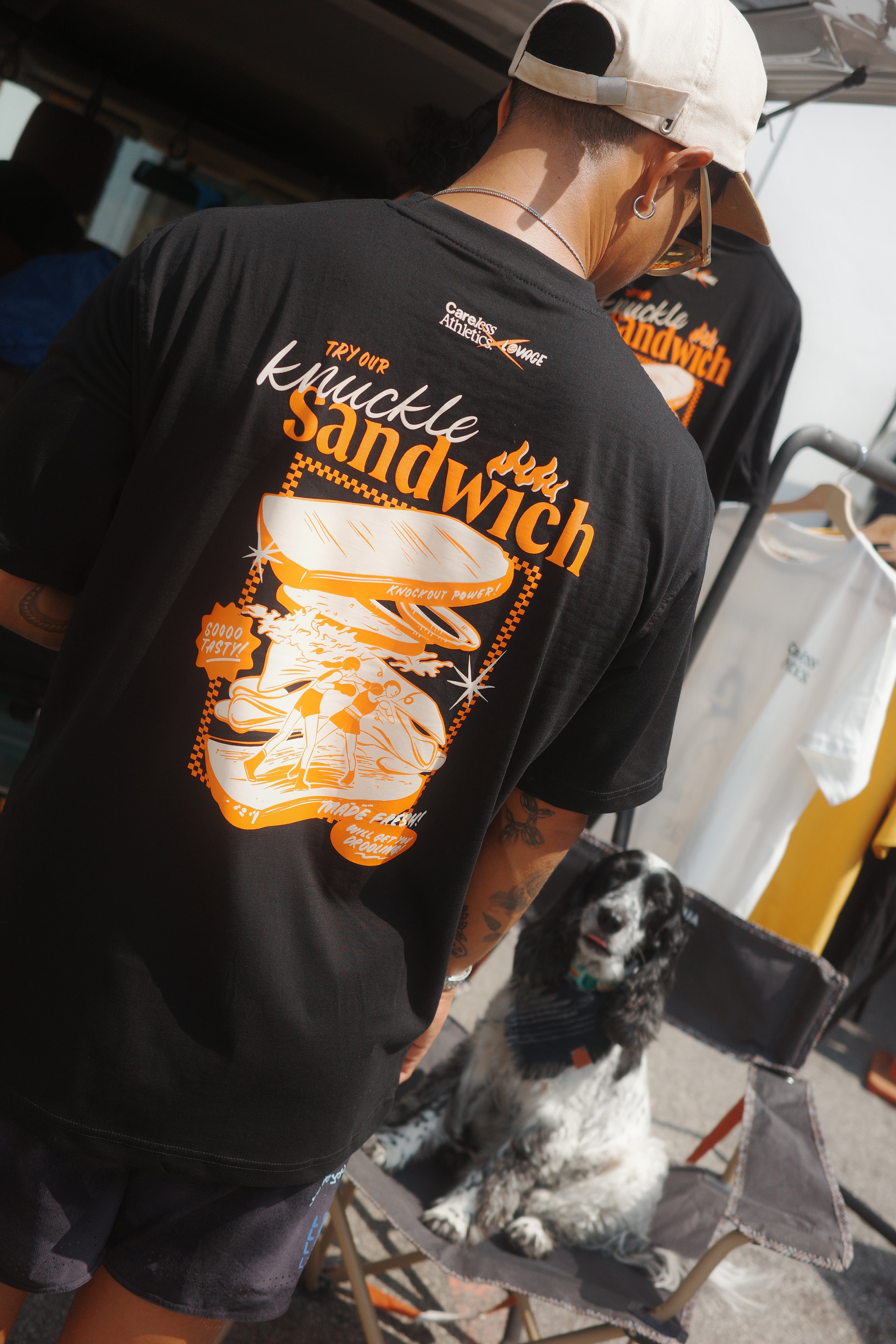 Person wearing a black t-shirt with a sandwich graphic and text, sitting on a chair.